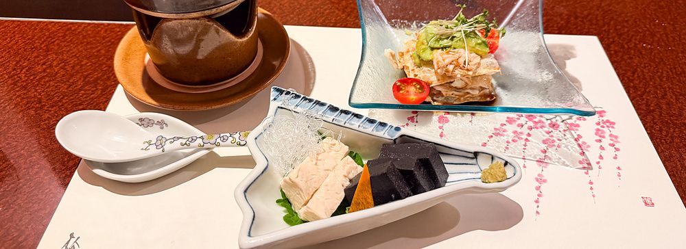 Antipasti a Ume no Hana a Ginza serviti in raffinati piatti di ceramica e vetro su una tovaglietta illustrata.