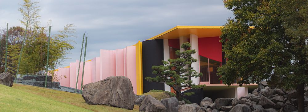 Edificio moderno dai colori accesi inserito in un parco con rocce, alberi e un prato inclinato in pendenza.