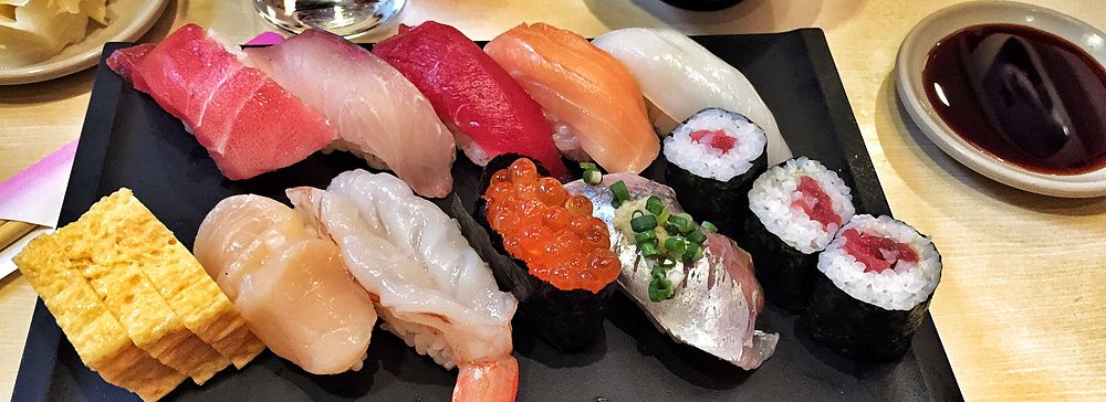 Assortimento di sushi con zuppa di miso su un tavolo di legno chiaro.