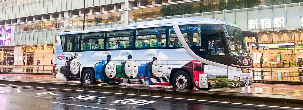 Autobus colorato davanti a Shinjuku South Exit, Tokyo, con edifici moderni sullo sfondo.