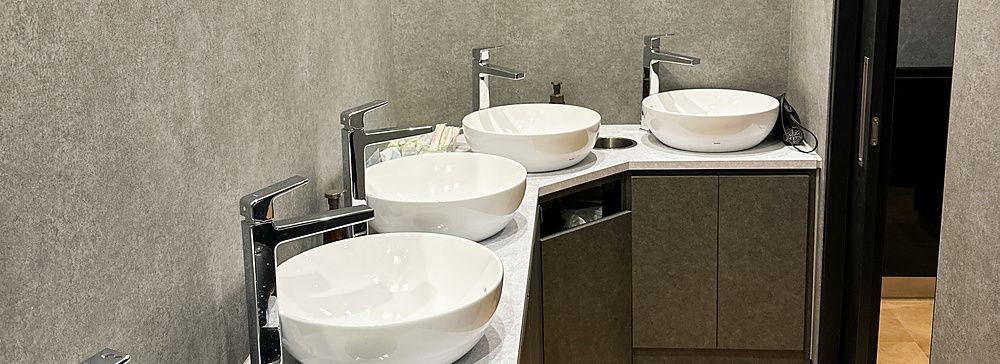 Bagno in comune con lavandini moderni, specchi rotondi e pareti grigie.