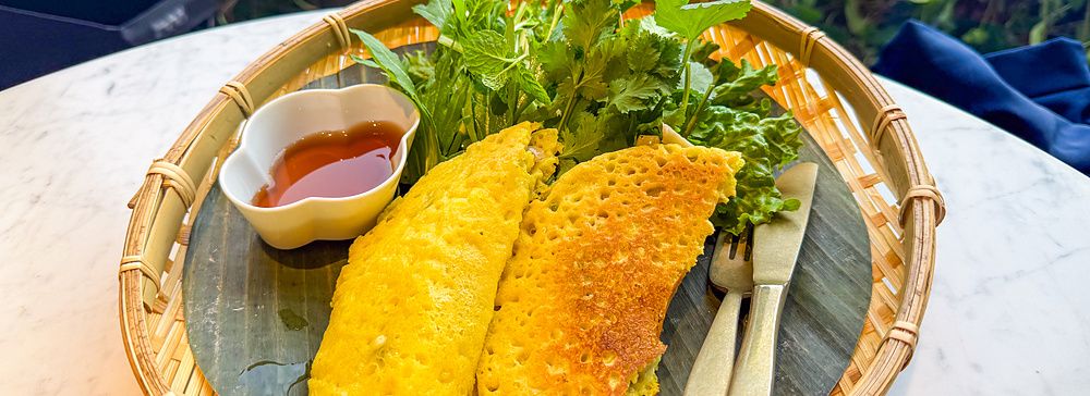 Un piatto di bánh xèo, crêpe vegana, servito su una foglia di banano in un vassoio di vimini al Lotus Palace di Fukuoka.