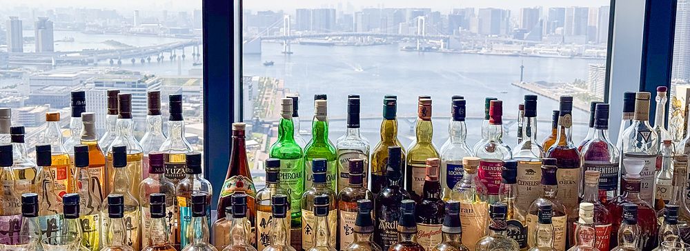 Bottiglie di whisky allineate sul bancone del bar nella lobby al Mitsui Garden Hotel Toyosu Premier con vista sulla baia.