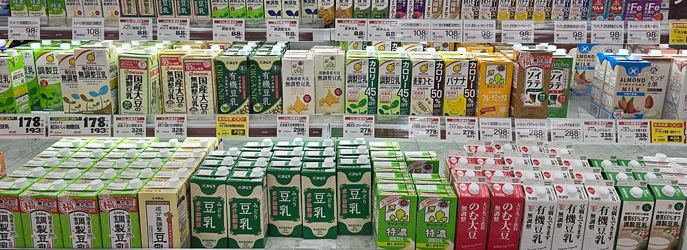 Scaffali refrigerati pieni di vari cartoni di latte vegetale in un supermercato in Giappone.