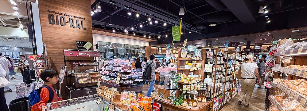 Interno del supermercato Bio-Ral con scaffalature in legno e clienti tra le corsie di prodotti biologici.