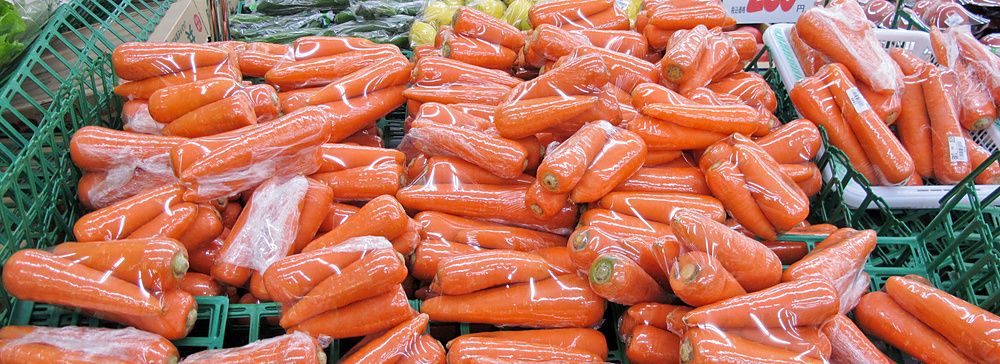 Carote confezionate su scaffali in un supermercato giapponese con cartelli dei prezzi.