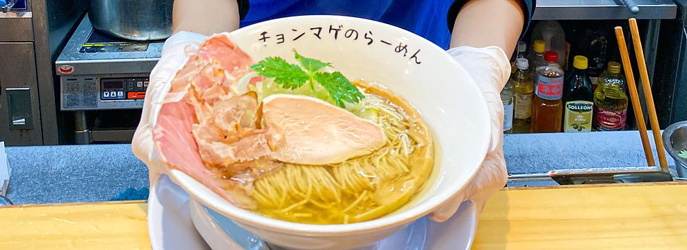 La chef a Ramen Chonmage Osaka Tenroku Ten sorride tenendo una ciotola di ramen preparata nel ristorante.