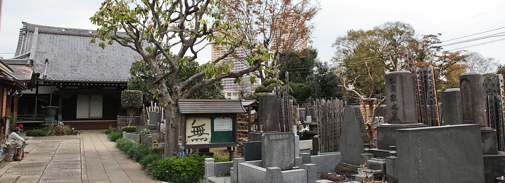 Veduta del cimitero a Yanaka a Yanaka, con lapidi in pietra, un sentiero lastricato e un tempio sullo sfondo.