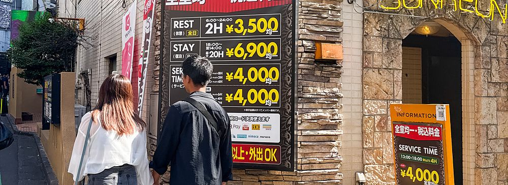 Una coppia passeggia davanti a un hotel con insegne luminose a Shibuya.