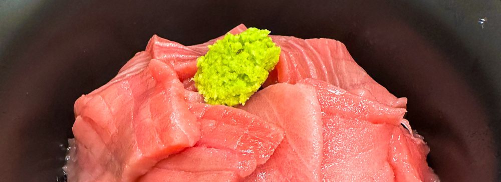 Una ciotola nera contenente fette di tonno crudo e wasabi su una base di riso servita presso Maguro Koya a Nara.