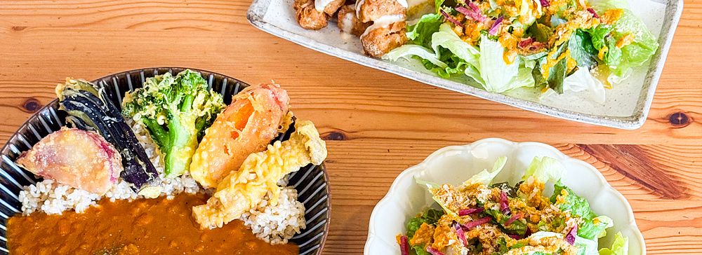 Piatti di curry, insalata, falafel e molto altro a Marugoto, ristorante vegano ad Asakusa, su un tavolo di legno.