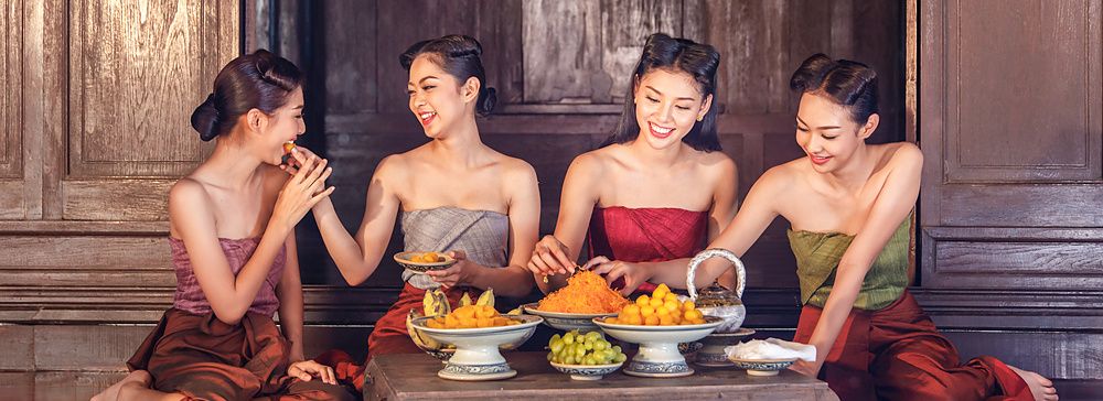 Donne in abiti tradizionali tailandesi mangiano dessert insieme.