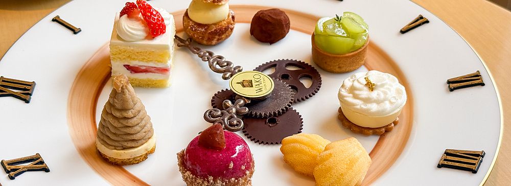 Una selezione di dolci su piatto a forma di orologio a Wako Tea Salon con numeri romani e lancette decorative.