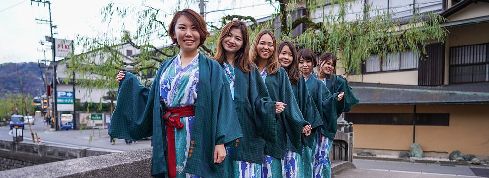 Gruppo di donne in yukata posano in fila su un ponte di pietra a Kinosaki Onsen in Giappone.