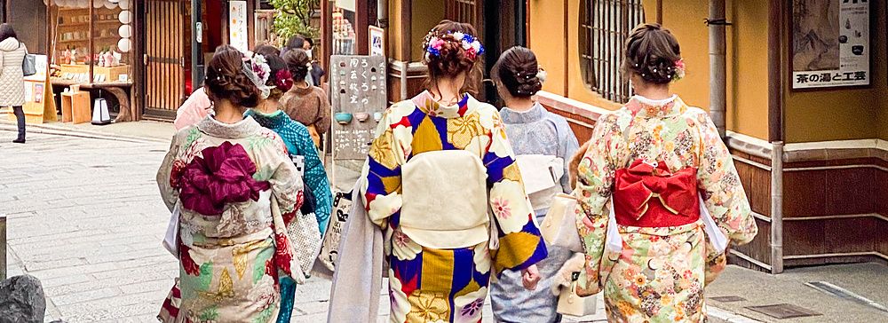 Quattro persone in kimono camminano di spalle lungo una via in pietra nel quartiere di Higashiyama a Kyoto.