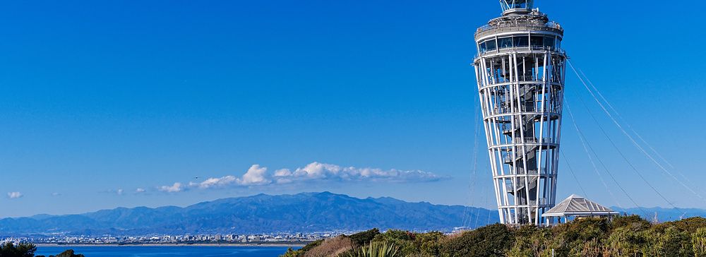 Veduta della torre Enoshima Sea Candle su un colle affacciato sull'oceano in una giornata di sole con cielo blu.