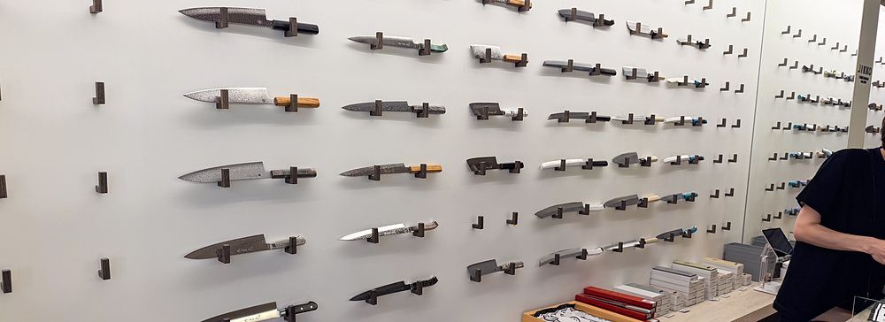 Un'esposizione coltelli a Jikko ad Osaka con lame artigianali fissate alla parete e accessori sul bancone.