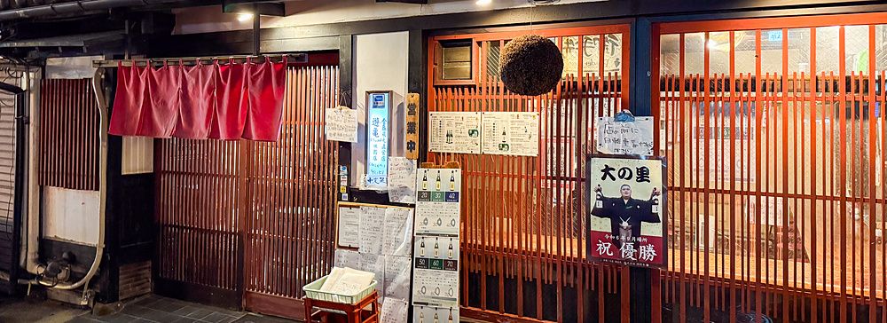 L'esterno di Gion Yuki a Kyoto presenta una facciata in legno scuro con infissi a listelli rossi e insegne informative.