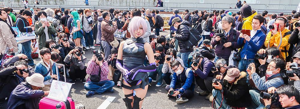 Persona in cosplay circondata da numerosi fotografi durante un evento.