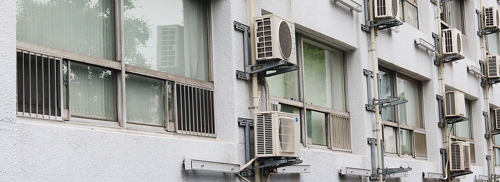 Facciata di un edificio residenziale a Tokyo con numerose unità esterne di condizionatori installate in serie.