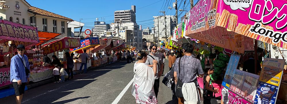 Bancarelle di cibo colorate lungo una strada di Hiroshima durante un festival locale con persone che camminano.