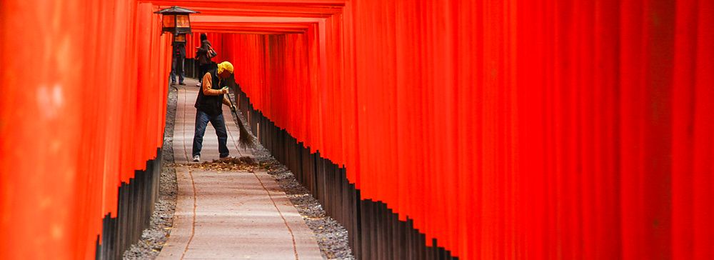Una persona pulisce il sentiero tra i torii rossi di Fushimi Inari.