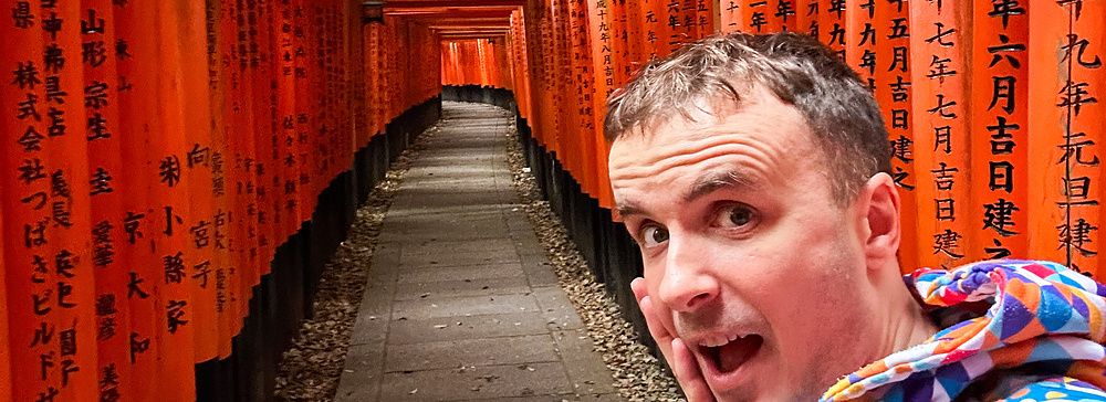 Marco Togni in giacca colorata tra i torii di Fushimi Inari a Kyoto.