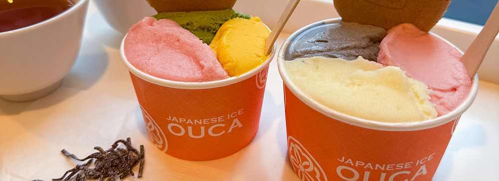 Due coppette di gelato con logo Ouca su un tavolo accanto a una vetrina che affaccia su una strada a Ebisu, Tokyo.