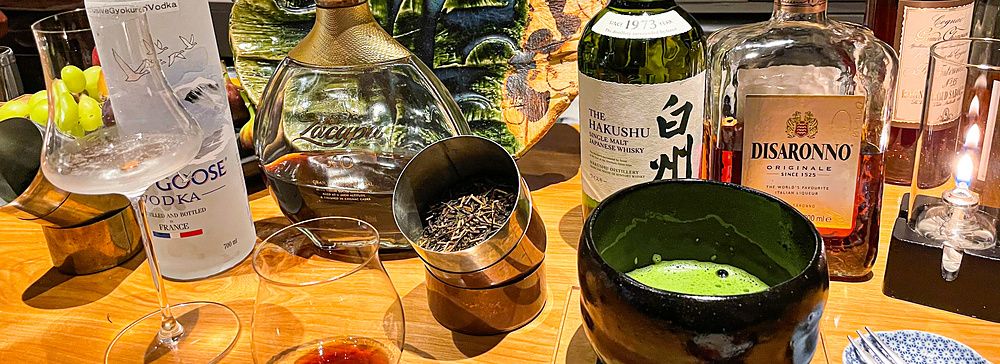 Bottiglie di alcolici, una ciotola di matcha e un piatto decorativo sul bancone in legno del Mixology Salon a Ginza.