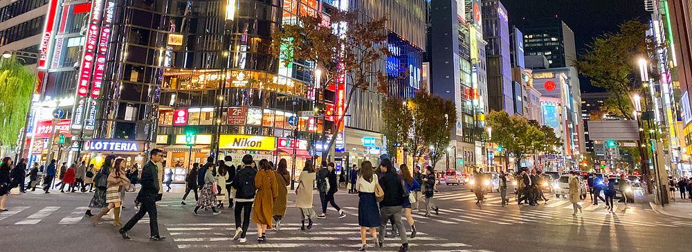 Strada affollata di notte a Ginza con luci al neon e cartelloni.
