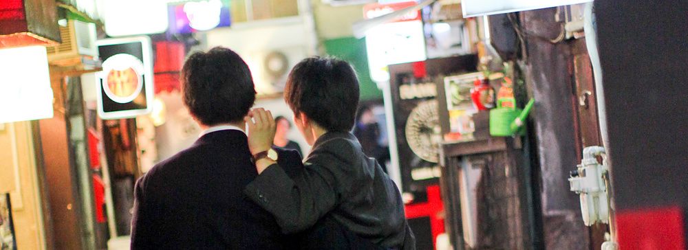 Due uomini camminano in un vicolo illuminato da insegne al neon a Golden Gai, Tokyo.
