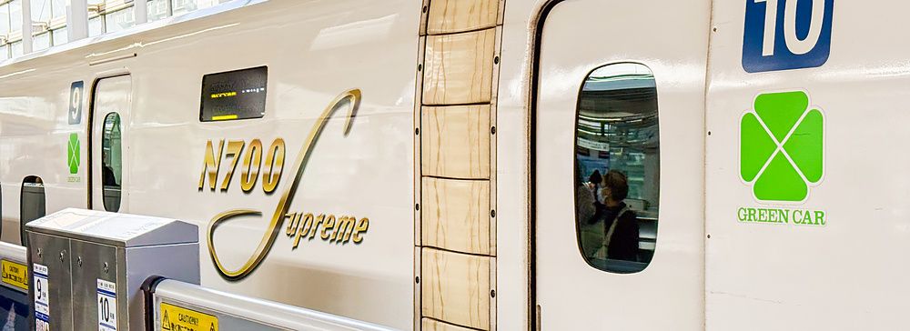 Un treno Shinkansen N700 Supreme bianco con il simbolo della Green Car e il numero 10 su una banchina ferroviaria.