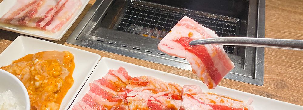 Una fetta di carne cruda sollevata con le bacchette sopra una griglia presso il ristorante Yakiniku Like.
