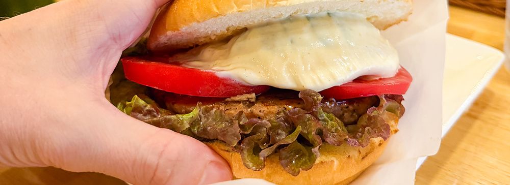 Una mano tiene un hamburger vegano farcito con pomodoro e lattuga servito nel ristorante Komeda Is a Ginza.