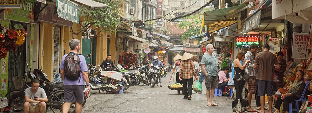 Strada di Hanoi con pedoni, motorini e negozi animati.