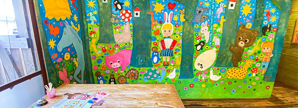 Un tavolo di legno in una stanza del ristorante Hattifnatt a Kichijoji, con una parete dipinta con personaggi colorati.