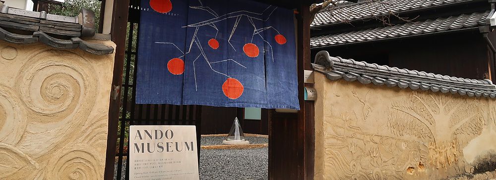 Ingresso dell'Ando Museum a Naoshima con cancello, noren blu decorato e parete in stucco lavorato.