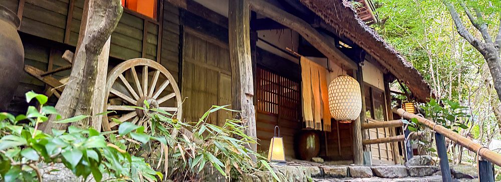 L'ingresso del ristorante a Kurochaya, con scalinata in pietra, struttura in legno e lanterne in un bosco di Akiruno.