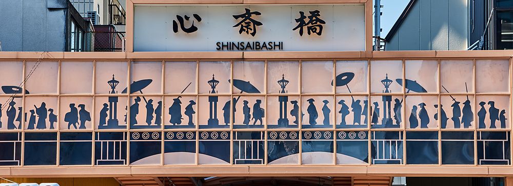 Insegna decorata dell'ingresso di Shinsaibashi a Osaka con silhouette di persone e caratteri giapponesi.