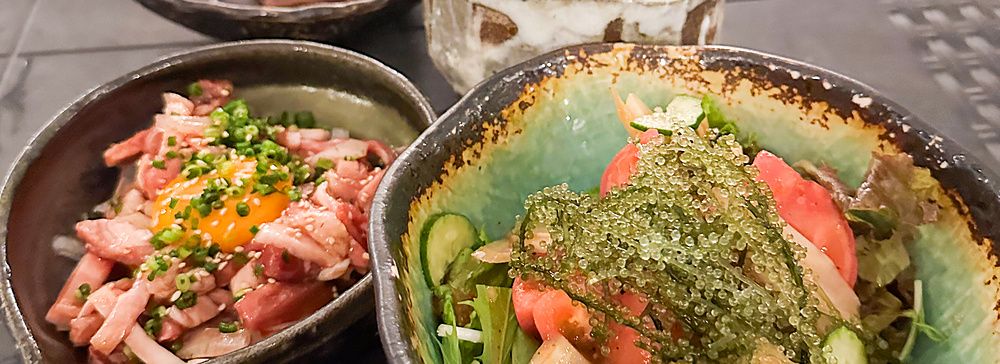 Insalata di umibudo e yukhoe di carne serviti in ciotole di ceramica su un tavolo da Izakaya Ichitaka a Iriomote.
