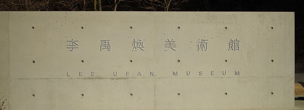Parete in cemento a vista con scritte incise del Lee Ufan Museum in un'area esterna in Giappone.