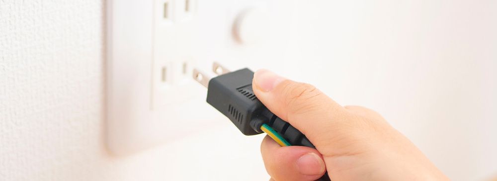 Mano che inserisce una spina elettrica nera in una presa a muro bianca.