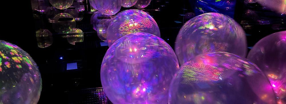 Installazione artistica con sfere traslucide illuminate da luci colorate in una sala oscura a Kyoto.