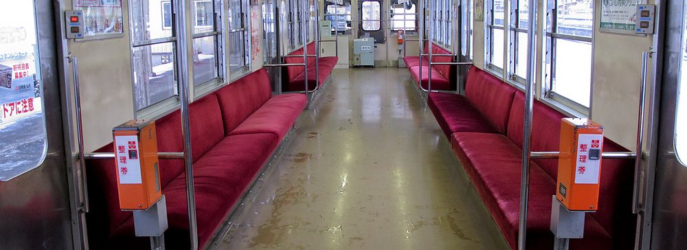 Interno di un treno giapponese con sedili rossi e appigli a soffitto vuoti