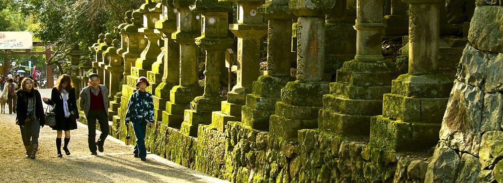 Turisti camminano accanto a lanterne di pietra con muschio al santuario Kasuga Taisha, Nara.