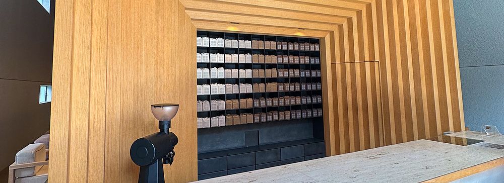 Veduta interna di Koffee Mameya Kakeru a Tokyo con bancone in pietra e una parete espositiva in legno per il caffè.