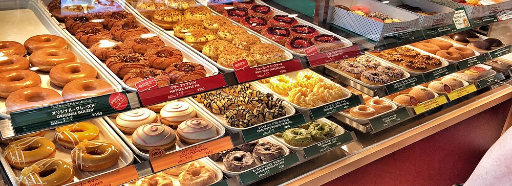 Espositore di ciambelle assortite all'interno di un negozio Krispy Kreme a Tokyo con una persona visibile.