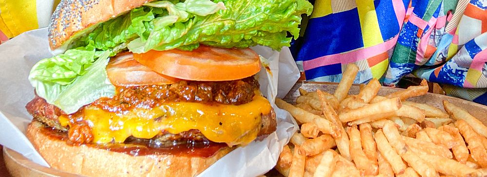 Marco Togni con occhiali rosa morde un hamburger in un ristorante.