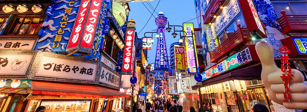 Strada animata di Shinsekai a Osaka con una grande lanterna a forma di pesce palla e la torre Tsutenkaku sullo sfondo.