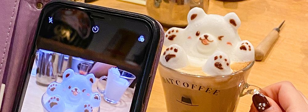 Una persona fotografa con lo smartphone una tazza di cappuccino con latte art a forma di orso presso Hatcoffee ad Asakusa.